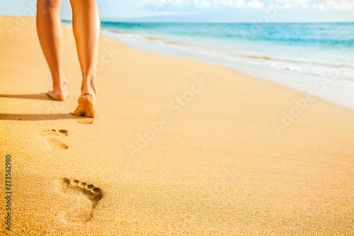 Beach woman legs feet walking barefoot on sand leaving footprints on golden sand in sunset. Vacation travel freedom people relaxing in summer. photo