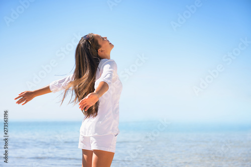 Happy woman happiness emotion feeling free in summer sun lifestyle background. Joy and freedom concept. Asian girl with outstretched arms at beach ocean vacation travel.