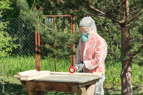 Woman carpenter in respirator, goggles and overalls handles a wooden board with a Angle grinder photo