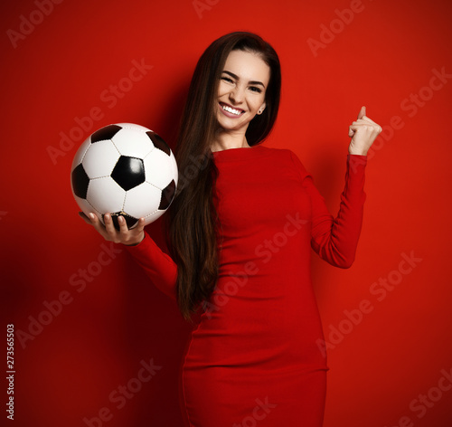 Young pretty brunette woman in tight red dress with soccer ball in her hand looks up celebrating a win photo