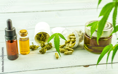 CBD cannabidiol oil glass bottles, pills flower buds and Cannabis leafs on bright wooden backdrop photo