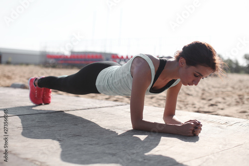 Close up of young pretty caucasian muscular woman doing plank exercise outndoor at the ground. Concept of health and sport lifestyle. Athletic Body of european girl...