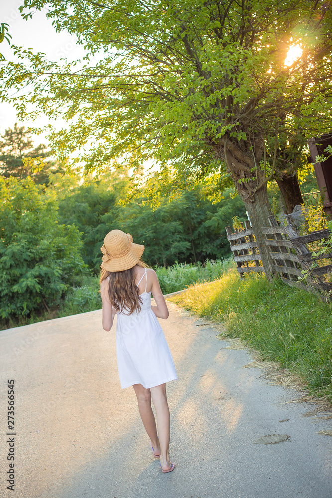 Cute young girl in white dress with yellow summer hat walking. Vacation concept