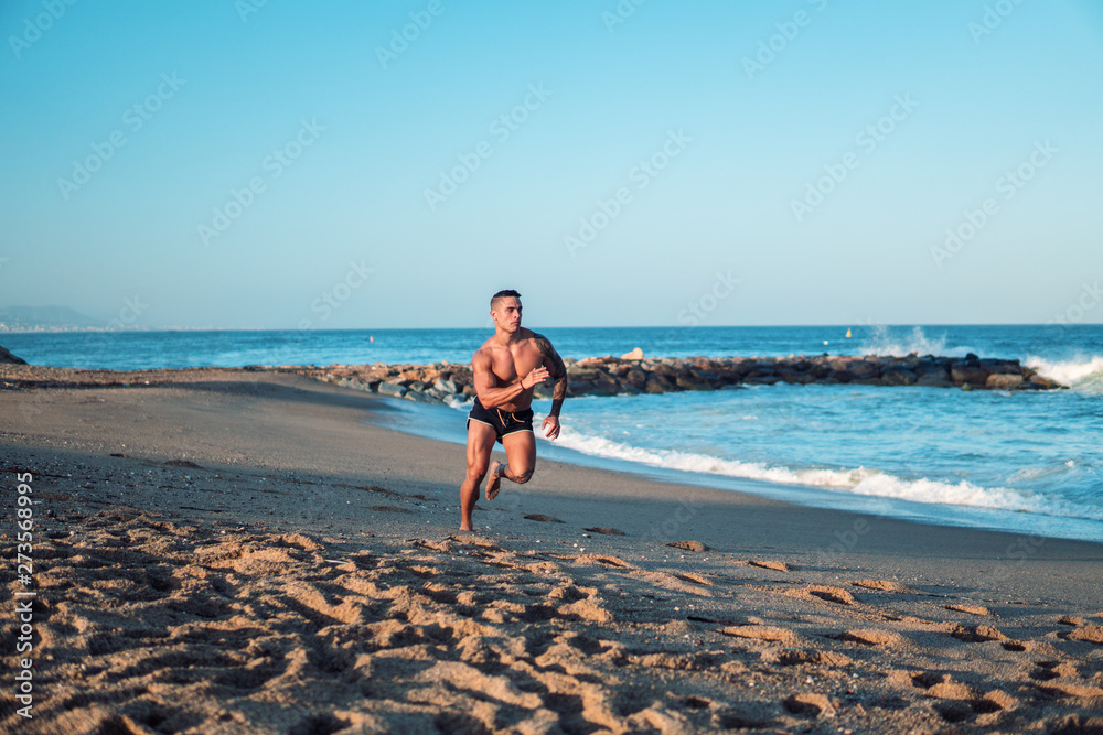 Tattooed bodybuilder sexy male coach at the beach. He runs and shows mucles