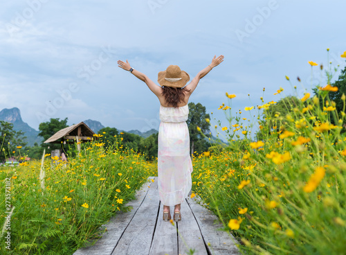 woman with arm raised on wooden bridge with yellow cosmos flower field