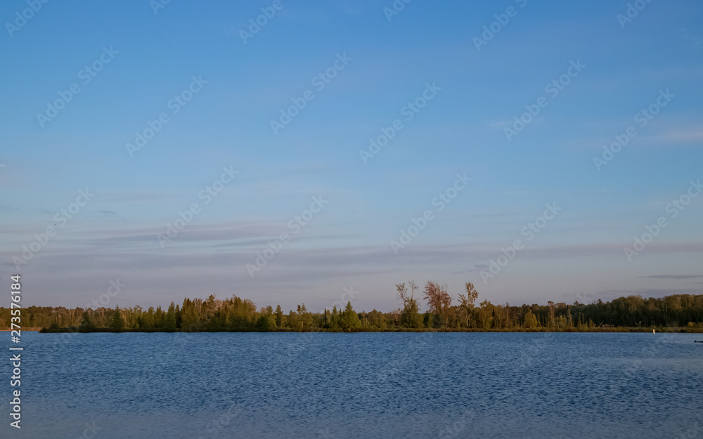 View of the Chippewa Flowage  with Northwoods deciduous and coniferous trees against sunset sky