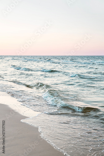 Fototapeta Naklejka Na Ścianę i Meble -  seascape: white sandy beach and waves on the shore at dawn, subtle pastel-colored sunset sky in the background