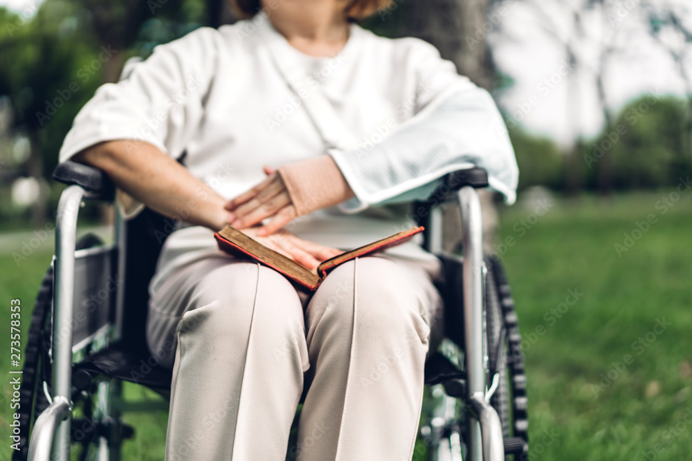 Obraz premium Senior adult elderly asia women sit on wheelchair and reading book outdoor