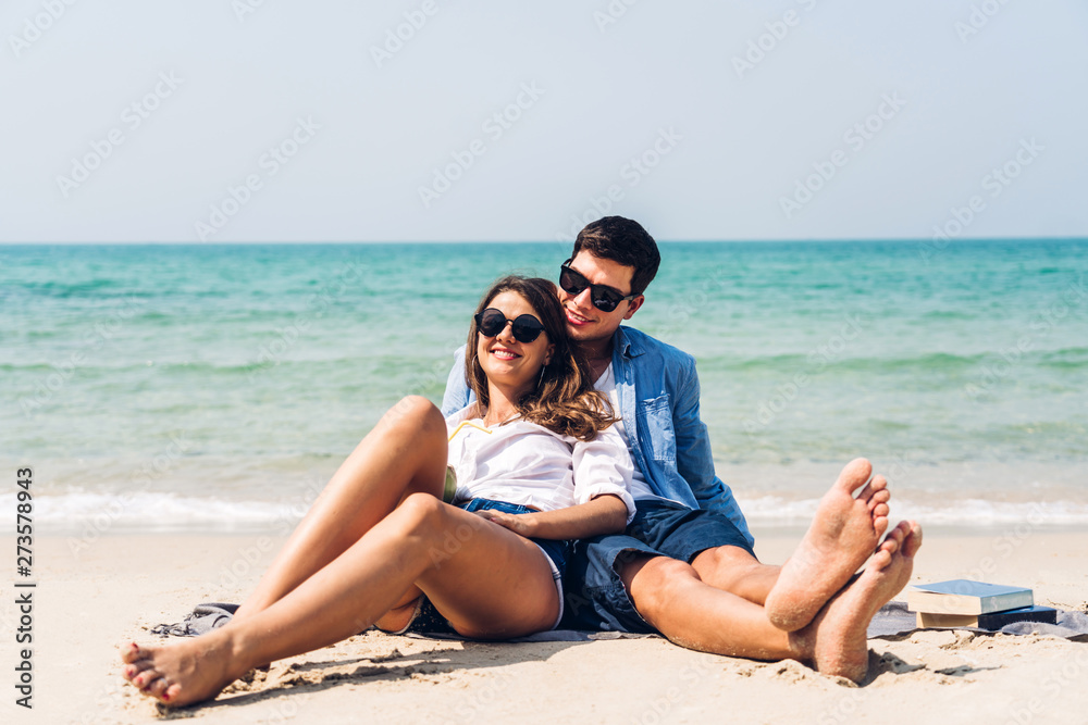 Young couple with coconut juice and book on the tropical beach.Couple relaxing on the beach.Summer vacations Young couple with coconut juice and book on the tropical beach.Couple relaxing on the beach.Summer vacations
