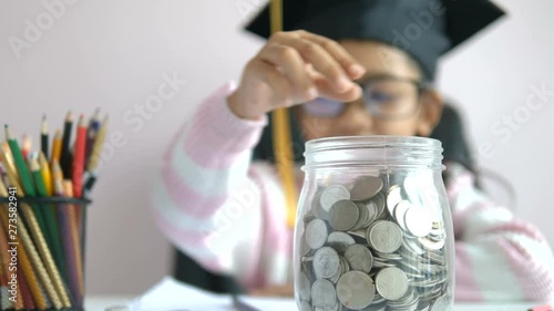 Little Asian girl puttinwg the coin into piggy bank and smile with happiness for money saving to wealthness in the future of education concept select focus shallow depth of field photo