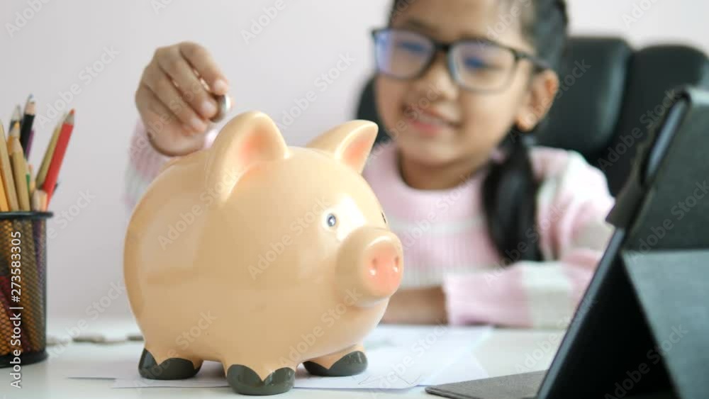 Little Asian girl puttinwg the coin into piggy bank and smile with happiness for money saving to wealthness in the future of education concept select focus shallow depth of field Little Asian girl puttinwg the coin into piggy bank and smile with happiness for money saving to wealthness in the future of education concept select focus shallow depth of field