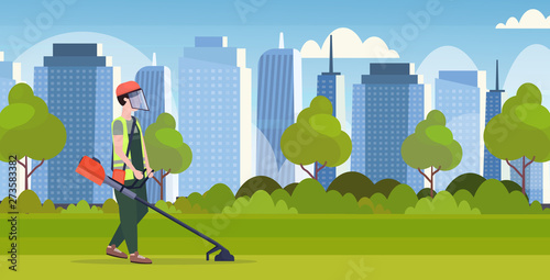 man gardener in uniform cutting grass with brush cutter gardening concept modern cityscape background full length flat horizontal