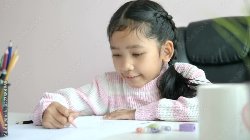 Little Asian girl using the pencil to write on the paper doing homework and smile with happiness for education concept select focus shallow depth of field Little Asian girl using the pencil to write on the paper doing homework and smile with happiness for education concept select focus shallow depth of field