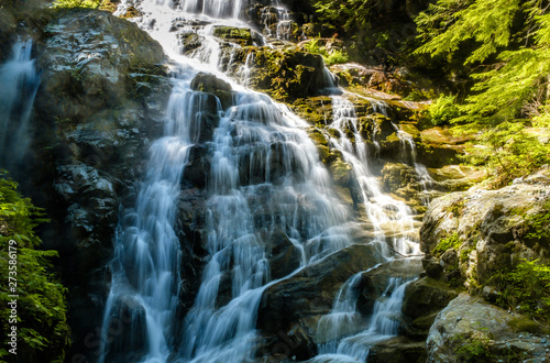 beautiful waterfall deep inside forest with sun illuminate the top and water running down the cascading creek on a hot summer day