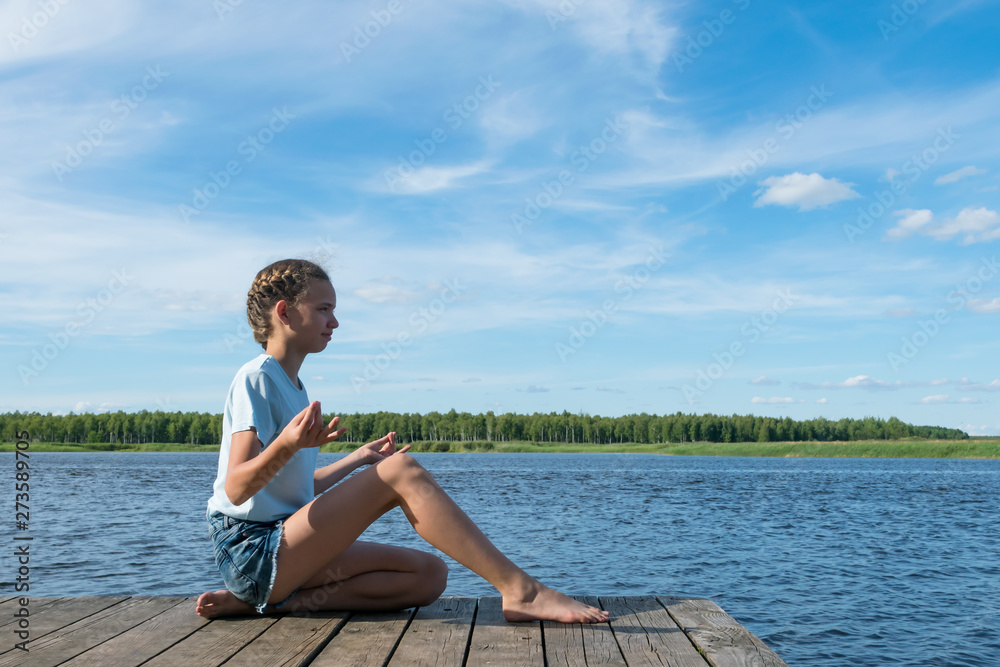 girl meditates in nature by the lake on a nice sunny day