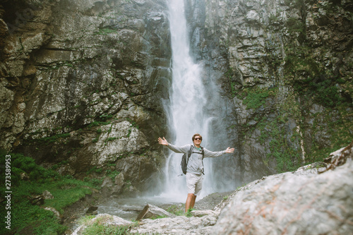 Young tourist man with his hands high near the waterfall Gergeti in Georgia