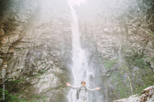 Young tourist man with his hands high near the waterfall Gergeti in Georgia