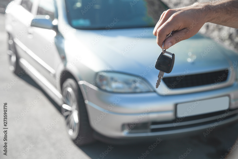 Man holding car key with car background.