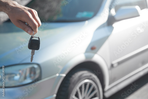 Man holding car key with car background.