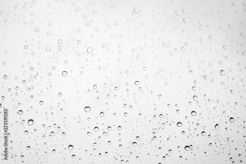 Window glass with drops of rain. Atmospheric light monochrome background with raindrops in bokeh. Droplets close up. Detailed black-white texture in macro with copy space. Rainy weather in grayscale.