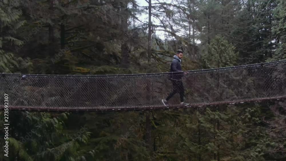 Man walking on suspension bridge, drone shot of man on suspension bridge. Capilano and Lynn valley canyon. Man walking on suspension bridge, drone shot of man on suspension bridge. Capilano and Lynn valley canyon.