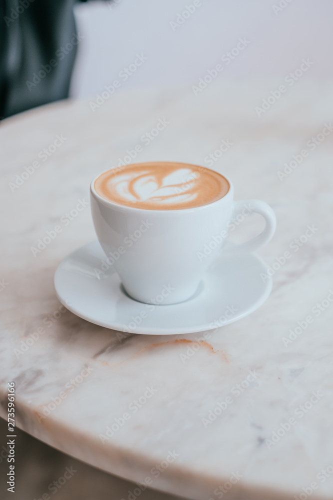 A cup of coffee with beautiful latte art in a white cup on marble table background. A cup of coffee with beautiful latte art in a white cup on marble table background.