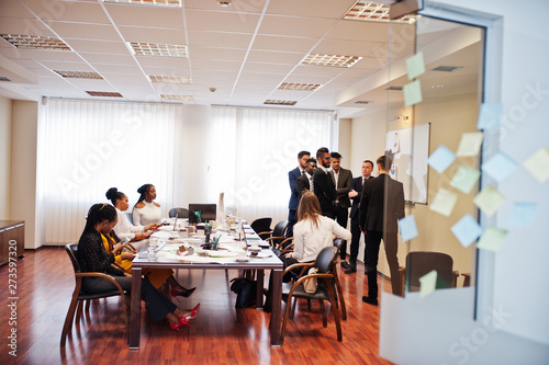 Multiracial business team addressing meeting around boardroom table and write plan on board.