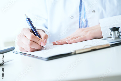 Female medicine doctor hand holding silver pen writing something on clipboard closeup.. Ward round, patient visit check, medical calculation and statistics concept. © cameravit