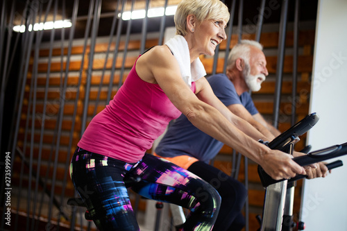 Happy fit mature woman and man cycling on exercise bikes to stay healthy