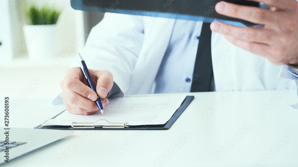 Close up of male doctor holding x-ray or roentgen image and making notes in medical form.