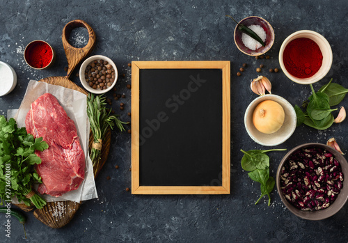 Fototapeta Naklejka Na Ścianę i Meble -  Cooking table with blank chalk board and beef meat, vegetables, spices, herbs top view. Food menu