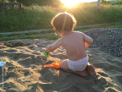 baby in the diaper plays with the sand, the sun shine over his head