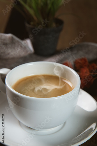 A cup of hot coffee  with coffee bean and milk cup on wooden table
