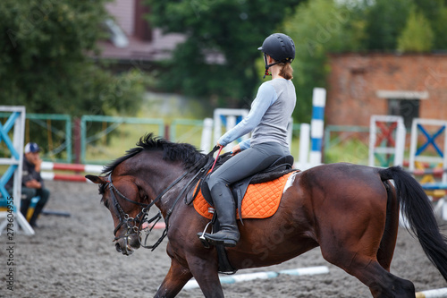 Young girl riding bay horse on show jumping training