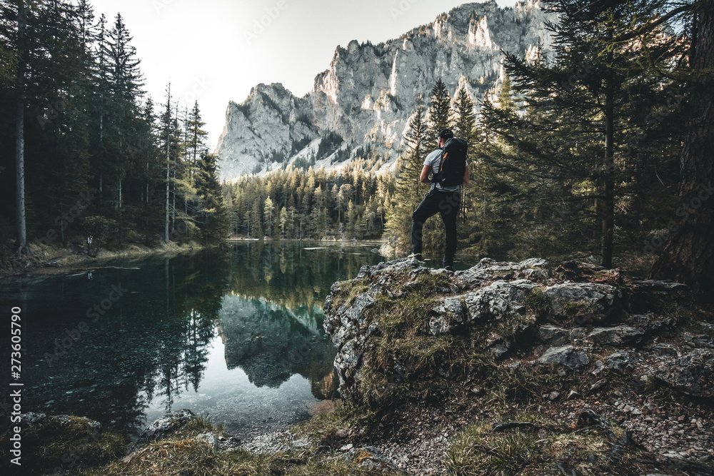 A man hiking to a lake and looking at the reflection of a mountain in austria