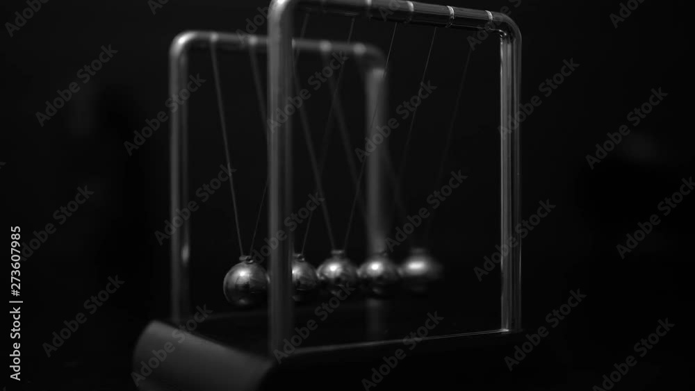 Newton's cradle in motion, five-ball system in one-ball swing. Left angle slow zoom in, black and white, slow motion, close up shot. Newton's cradle in motion, five-ball system in one-ball swing. Left angle slow zoom in, black and white, slow motion, close up shot.