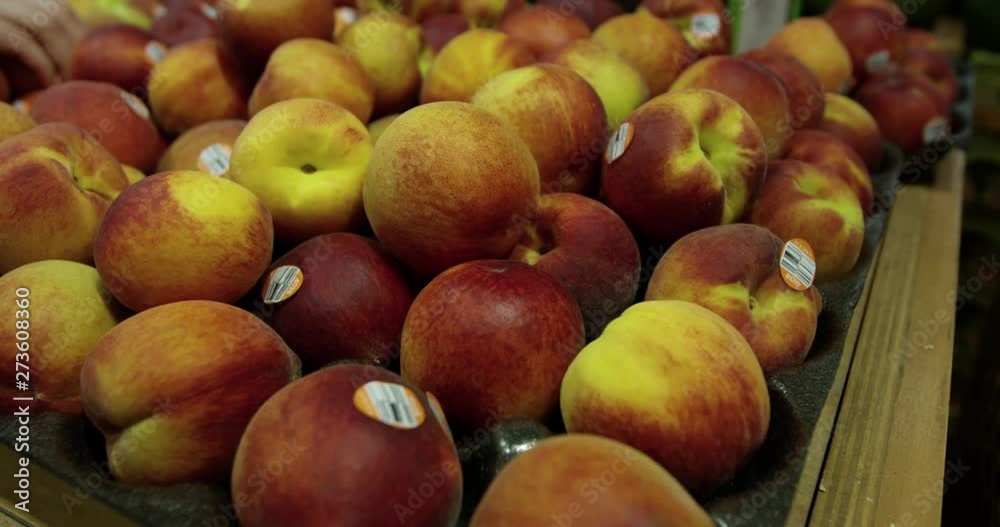 Peaches in grocery store - close up shot with hand grabbing one from the back Peaches in grocery store - close up shot with hand grabbing one from the back