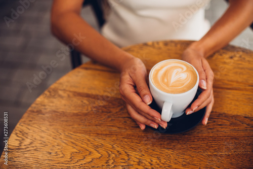 Woman holding cup of coffee cappuccino with heart shaped foam