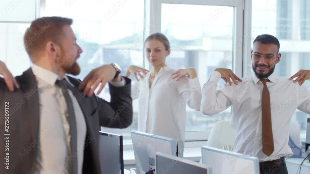 Tracking right of five multiethnic businesspeople standing at their desks and doing gymnastics together