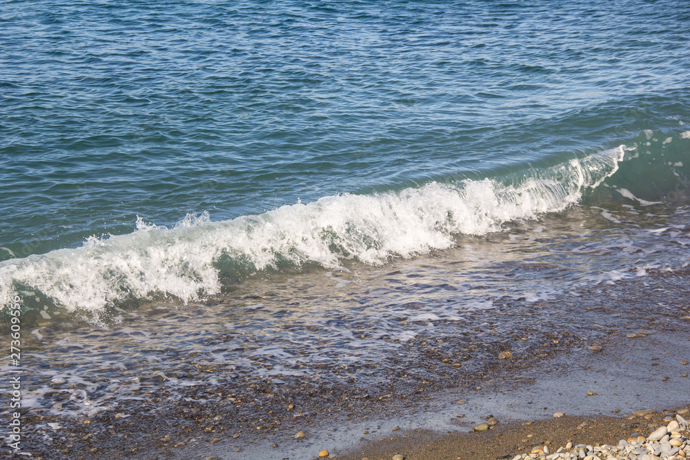 Fototapeta premium The sea foamy waves on an empty pebble beach