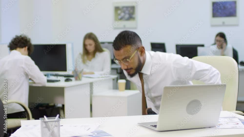 Medium shot of Arab businessman leaning on desk with his hands and doing push-ups while his colleagues working on background Medium shot of Arab businessman leaning on desk with his hands and doing push-ups while his colleagues working on background