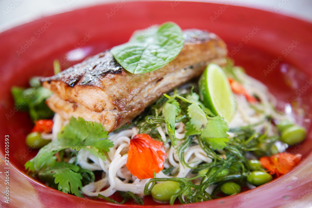 Grilled fish with green vegetable mix served in a red ceramic plate, casual healthy dining concept Grilled fish with green vegetable mix served in a red ceramic plate, casual healthy dining concept