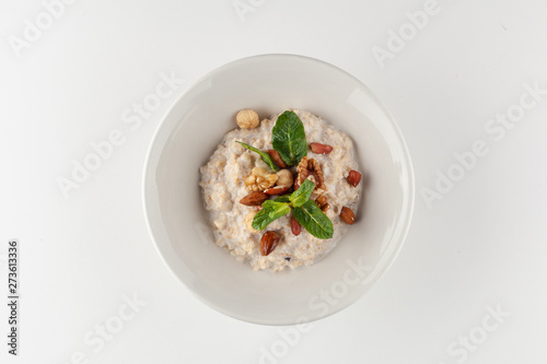 Oatmeal porridge with milk, almond, hazelnuts, honey and apple, decorated with mint leaves for a healthy breakfast, isolated on white