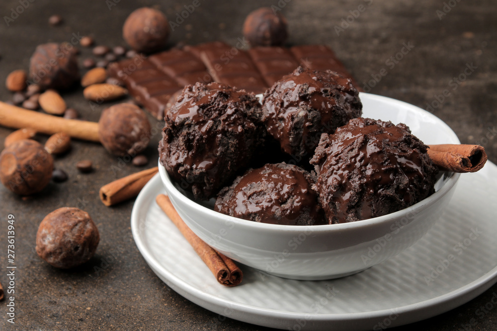 Chocolate ice cream with liquid chocolate with a cinnamon stick and coffee beans on a dark background. Chocolate ice cream with liquid chocolate with a cinnamon stick and coffee beans on a dark background.