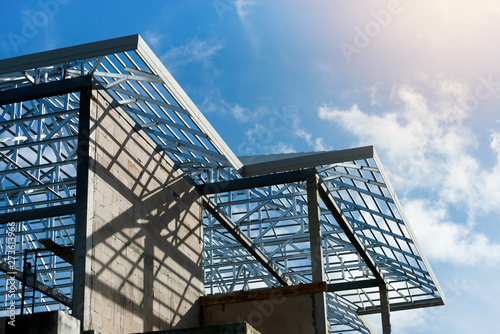 Roof frame of under construction house..Metal roof frame structure of a two story house without  roof tiles under sunny cloud blue sky,low angle view. © sbw19