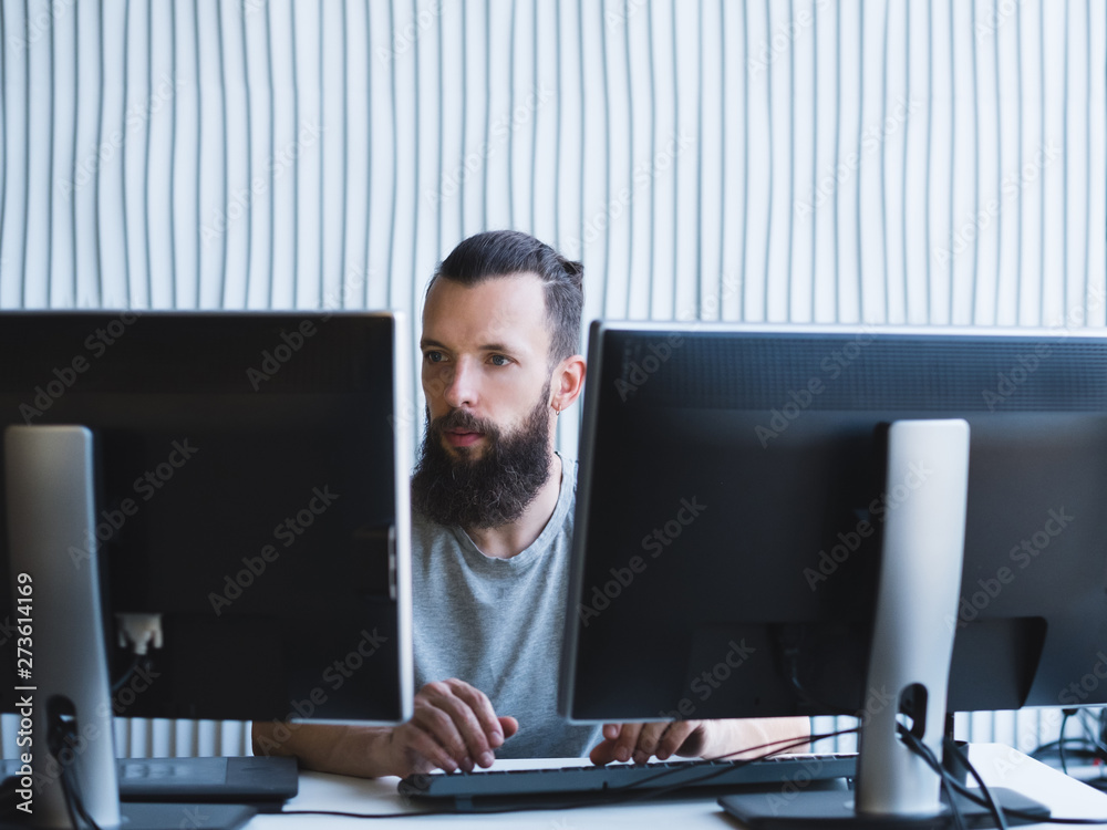 Quality assurance. Bearded software engineer using two monitors, working on task at office. Copy space. - obrazy, fototapety, plakaty 
