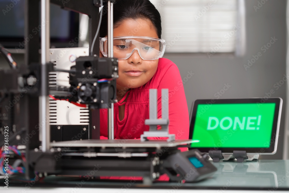 Young girl wearing protective glasses patiently waits for a 3d printer to finish printing her 3d design. Young girl wearing protective glasses patiently waits for a 3d printer to finish printing her 3d design.