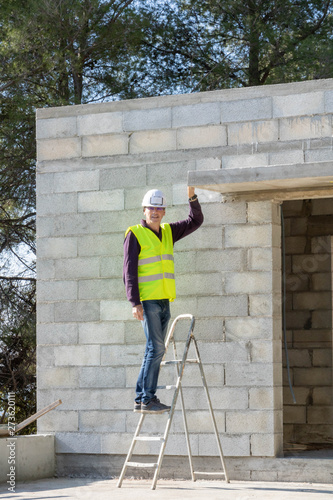 Chef de chantier en tenue de sécurité, sur une échelle maison en construction