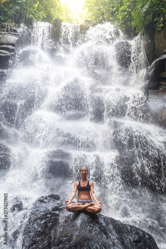 Woman practices yoga near waterfall in Bali  Indonesia