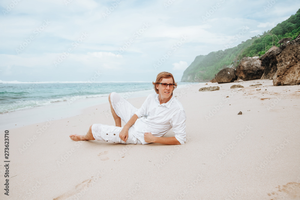 red-haired man in white clothes resting on a white beach